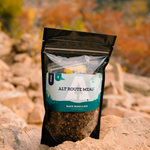 Photo of Alt Route Meals Black Beans and Rice dinner in package sitting on a rock with fall colors blurred in the background. 