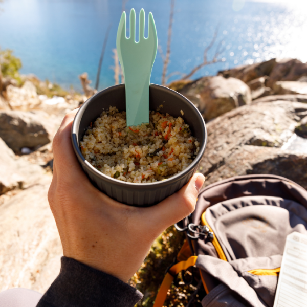 
                  
                    Alt Route Meals Veggie Fried Rice rehydrated in a cup. The cup is held in a hikers hand and has a spork sticking out of it. 
                  
                