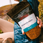 Photo of a woman hiker holding the Package of Thai Curry up to the camera. 