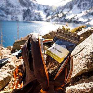 
                  
                    The Southwest Hash Brown Scramble is in its package falling out of a day pack. Day pack is resting on a rock on a boulder strewn lake front. Snowy mountains beyond the lake in the background. 
                  
                